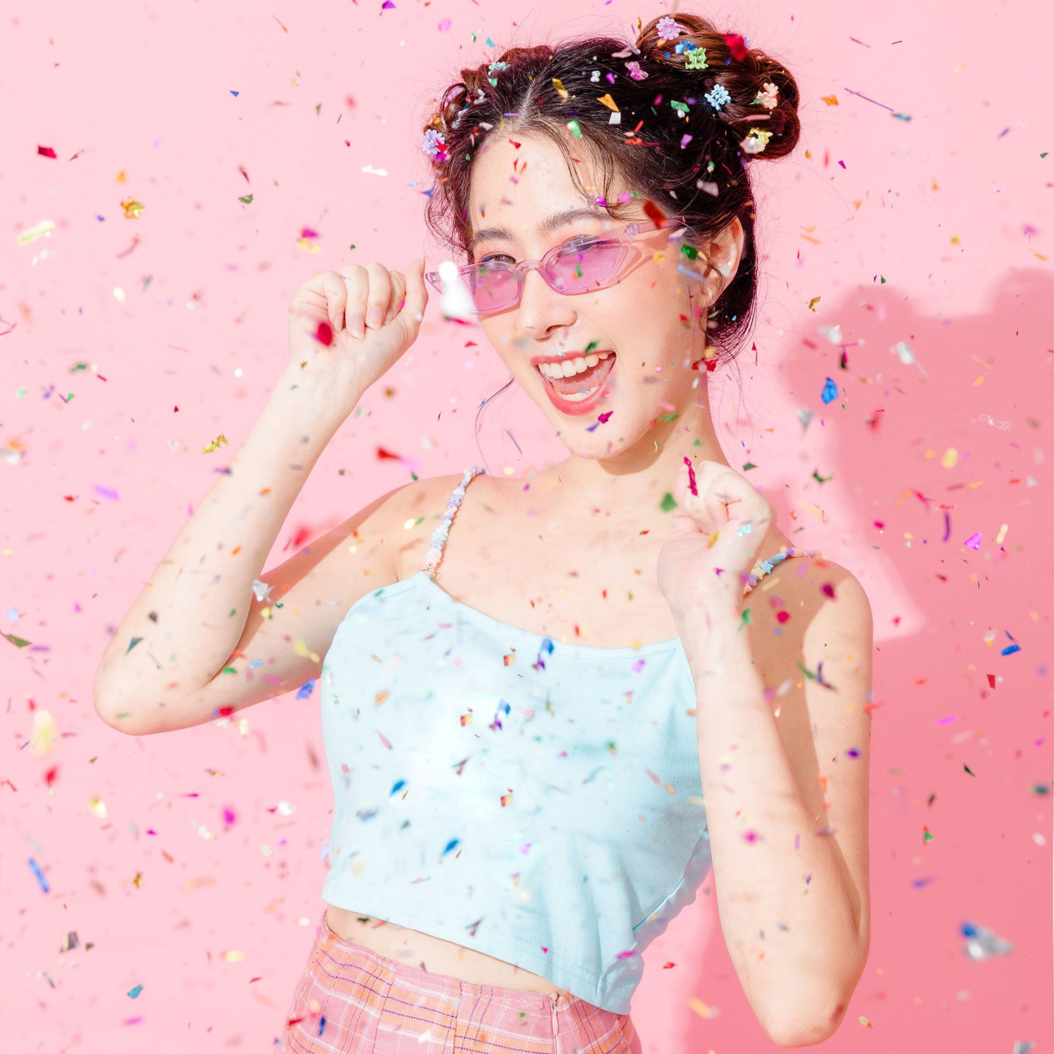 Woman with colorful confetti hair and clothing against a pink background