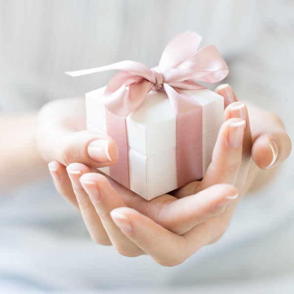 Small gift box with a pink ribbon held in hands against a light background