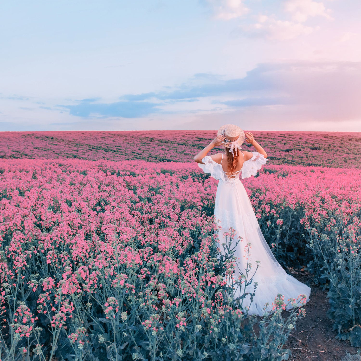 Woman in a white dress standing in a field of pink flowers with a blue sky.