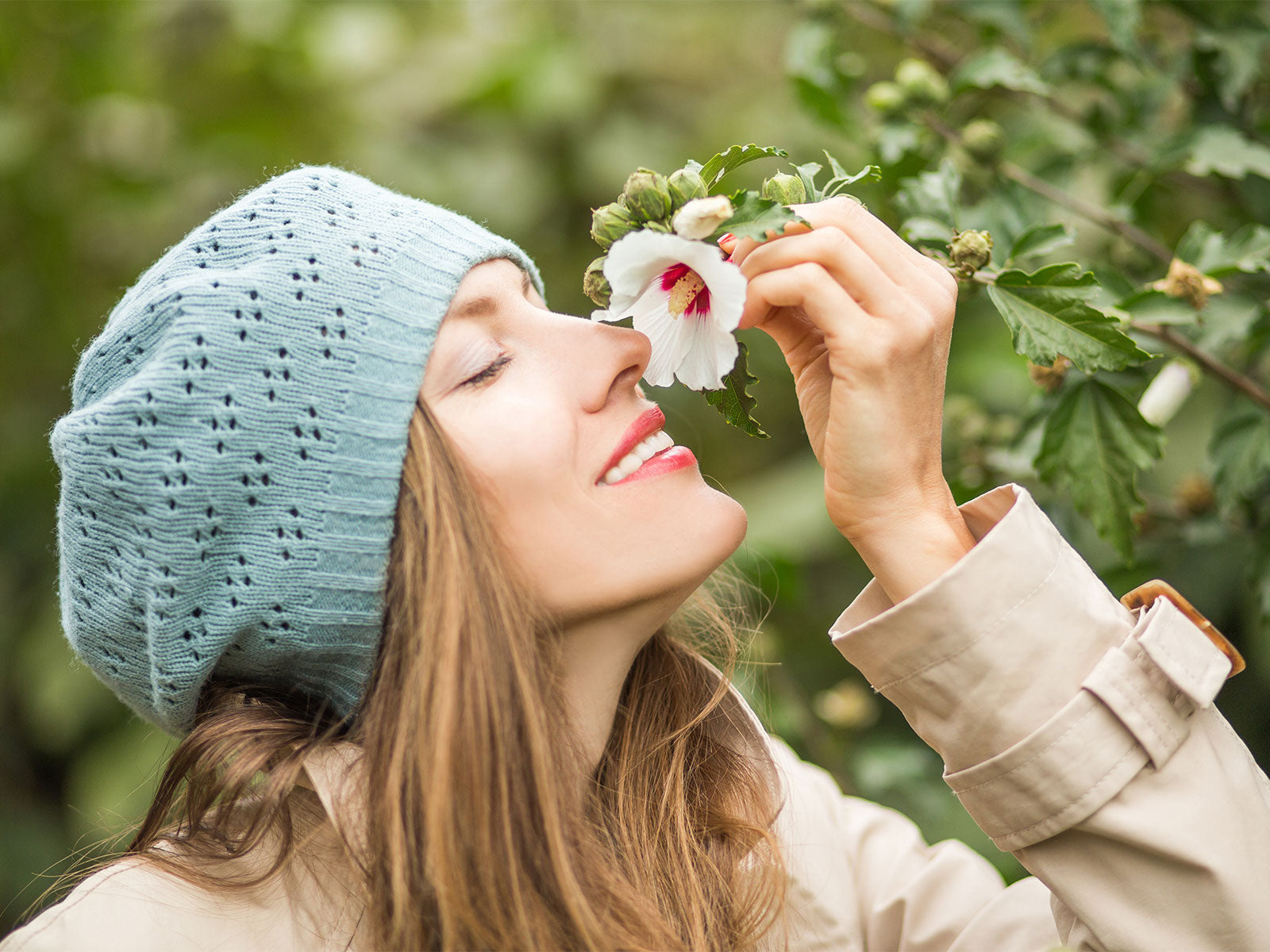 Woman smelling a white flower outdoors with greenery in the background